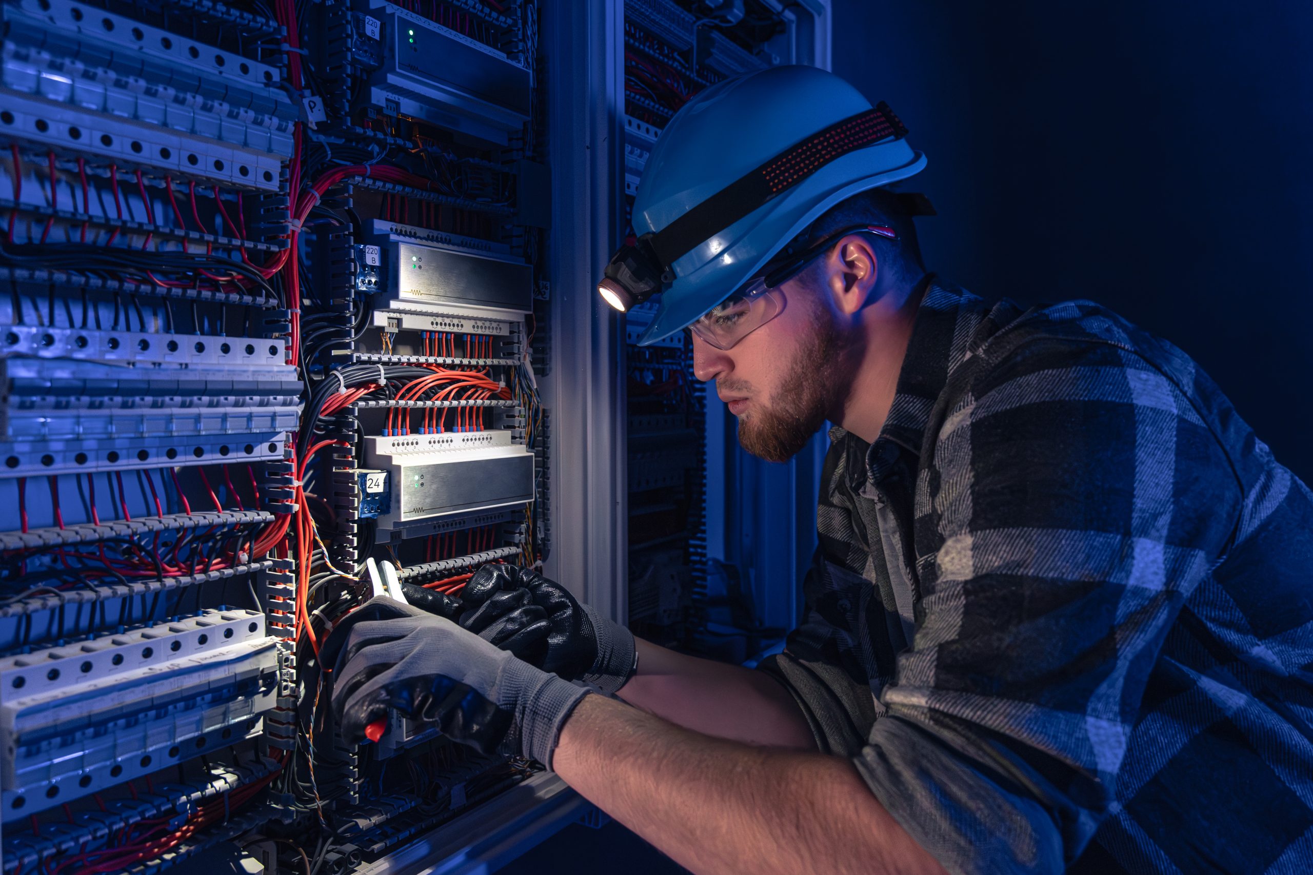 A male electrician works in a switchboard in overalls against the backdrop of emergency lighting. ITPro - IT Solution Divi Child Theme Image 21